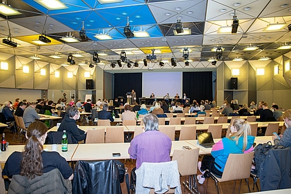 Die Konferenzhalle mit zahlreichen Teilnehmenden an Tischen 